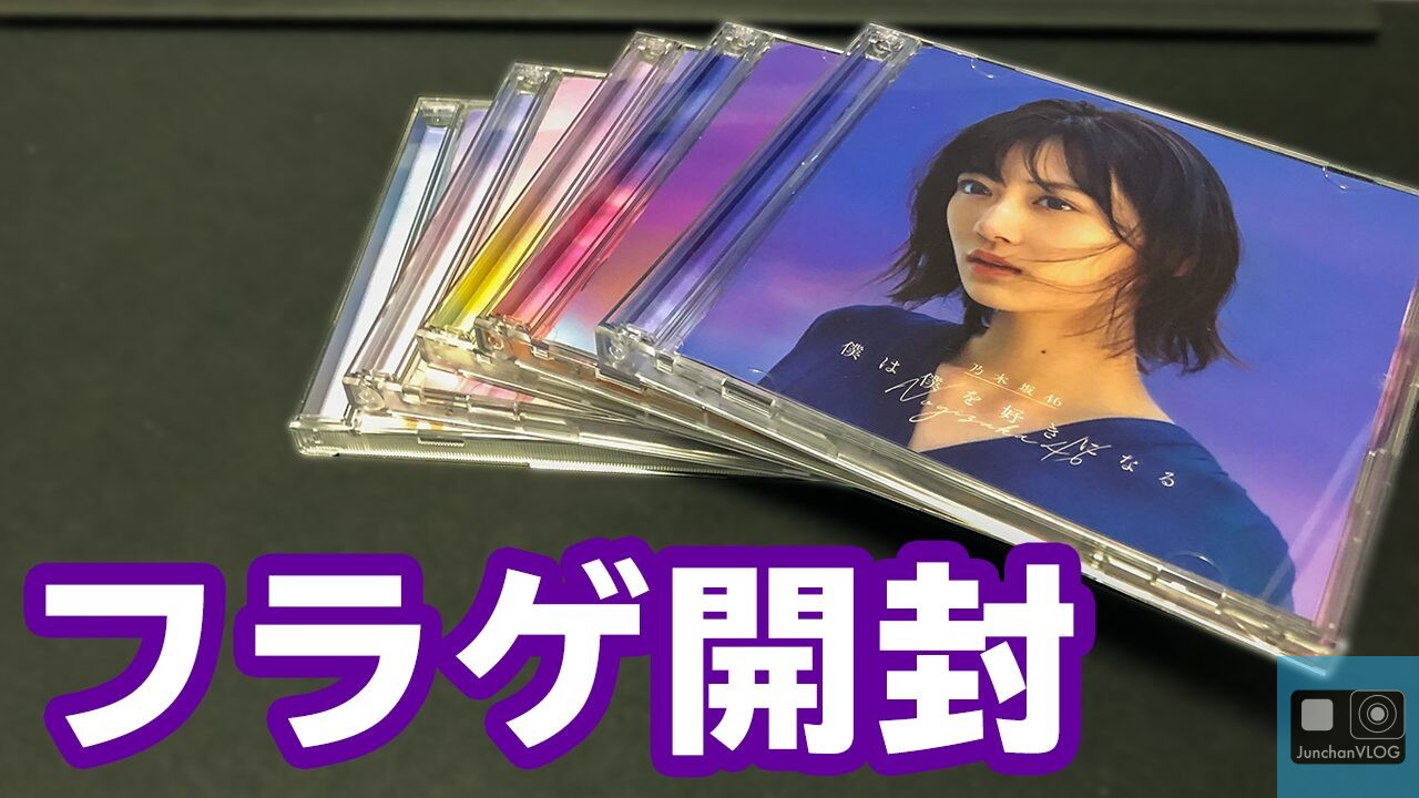 積み重ねられた CD ケース。一番上のカバーには女性が描かれています。CD は表面に広げられています。左下に太字の紫と白の文字で「フラグ開封」という日本語のテキストが表示されています。.
