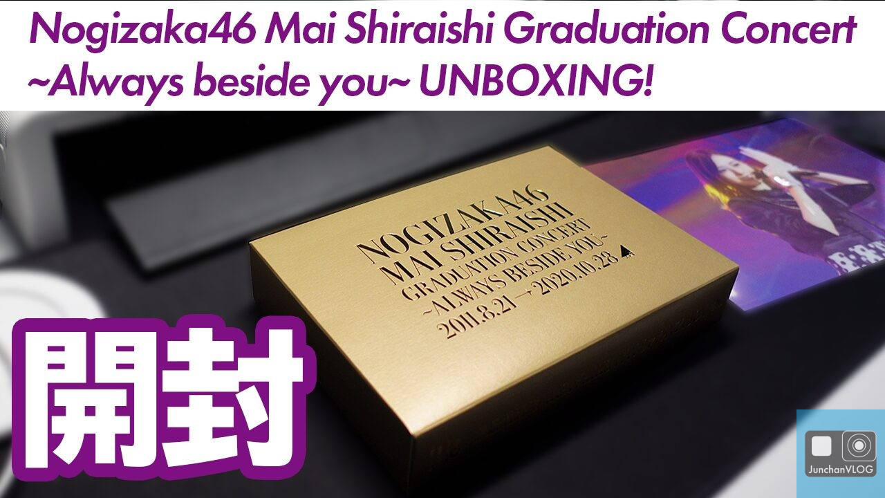 黒い表面に「乃木坂46 白石麻衣卒業コンサート ～Always beside you～」と書かれた金色の箱。背景にはステージで演奏している人物のぼやけた映像が描かれている。上部には紫と白の大きな文字で「UNBOXING!」と書かれている。.