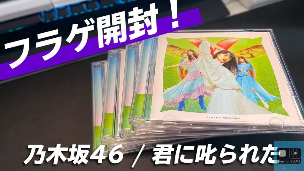 テーブルの上に CD アルバムが何枚か積み重ねられています。表紙には、翼の付いた色鮮やかなゆったりとした衣装を着た人々のグループが描かれています。CD 表紙の上部には太字の日本語のテキストが表示され、下部にも日本語のテキストが表示されています。.